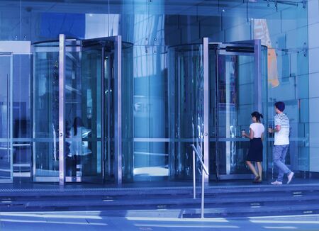 Office workers carrying coffee going into a building with glass revolving doorsの写真素材