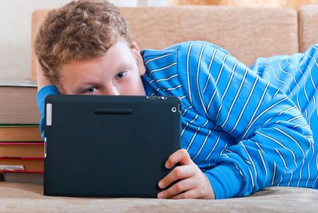Boy with a tablet computer lying on the sofaの写真素材