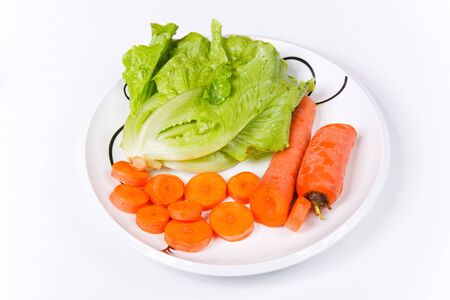 Well-cut carrots and green vegetable on a white porcelain dish on a white backgroundの写真素材