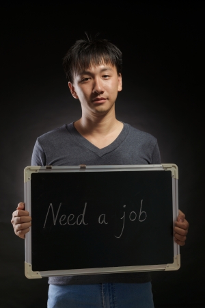 young asian man with a blackboard written "need a job" in photography studio with black backgroundの写真素材