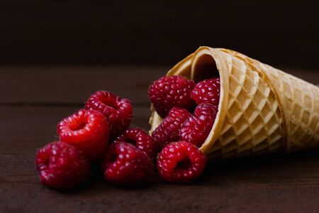 A cascade of fresh raspberries in a waffle cone of ice cream on a brown background. Cafe or restaurant menu. Close upの写真素材