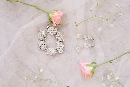 Bride's jewelry and rose flowers on white satin background. Earrings, bracelet on the air surface....