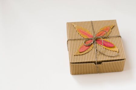 craft gift box, tied with string with a bow and autumn fallen leaves on a beige background. Copy spaceの写真素材