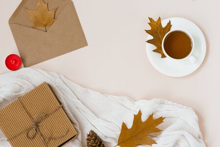 Autumnal flat lay with white knitted plaid, hot Cup of tea and fallen brown leaves, crab envelope, gift box. Top still life autumn concept on beige light background with copy space.の写真素材