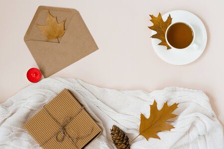 beautiful autumn composition with a Cup of tea. autumn leaves, Kraft gift box, an envelope and a knitted blanket on a beige background. the concept of the fall season. copy spaceの写真素材