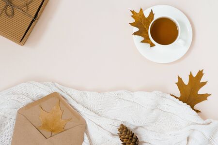 beautiful autumn composition with a Cup of tea. autumn leaves, Kraft gift box, an envelope and a knitted blanket on a beige background. the concept of the fall season. copy space. Autumn flat layの写真素材