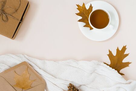 beautiful autumn composition with a Cup of tea. autumn leaves, Kraft gift box, an envelope and a knitted blanket on a beige background. the concept of the fall season. copy spaceの写真素材