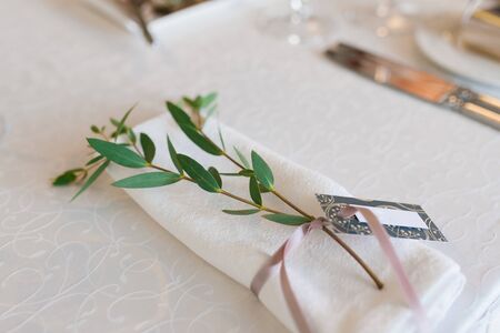 White dining napkin, tied with a dusty pink ribbon with branches of eucalyptus in the serving of the wedding Banquet tableの写真素材