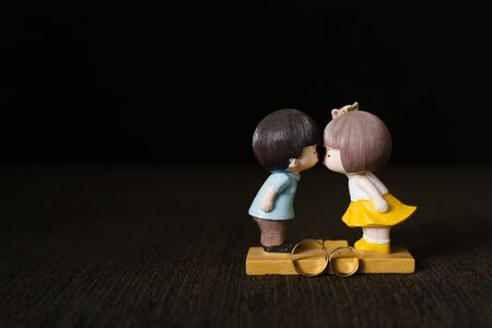 A statuette of a guy and a girl kissing and gold wedding rings on a brown backgroundの写真素材
