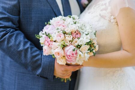 Delicate bouquet of the bride in the hands of the bride and groom, close-upの写真素材