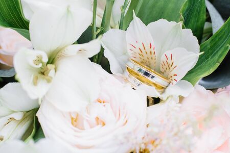 Wedding engagement rings of yellow and white gold are on the wedding bouquet, white flowersの写真素材