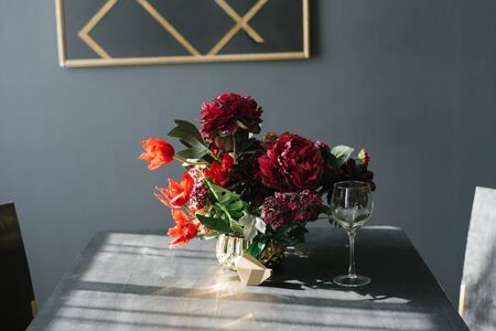 A bouquet of Burgundy flowers in a vase on the table in the living room or kitchen and a glass of wineの写真素材