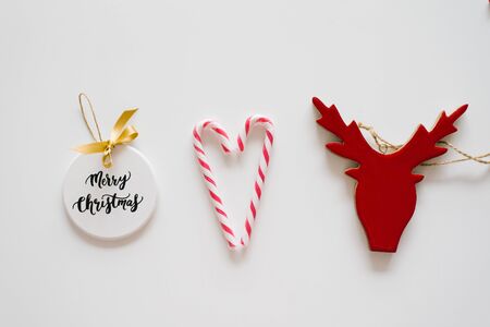 Christmas tree toys in the form of a red deer head and a white circle with the inscription "Merry Christmas" and two candy canes in the form of a heart on a white backgroundの写真素材