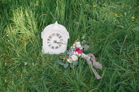 Classic table clock and wedding bouquet of the bride lie in the green grass. Wedding decorの写真素材