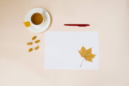 A white sheet of paper, a red pen, autumn leaves and a Cup of hot tea on a beige background. Copy spaceの写真素材