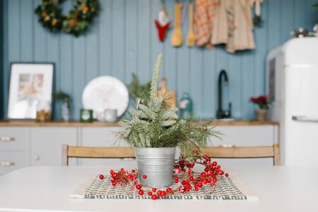 Fresh spruce branches or peonies or pines in a metal bucket, vase on the kitchen table in the decorated for Christmas and new year kitchen or living roomの写真素材