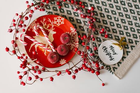 On red Christmas plate with deer lie red candied apples and candy cane, near lie line with red berries and Christmas toy. Christmas flat layの写真素材