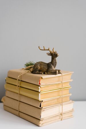 A stack of books in a craft cover, tied with twine, on the books is a statuette of a sitting deer on a gray backgroundの写真素材