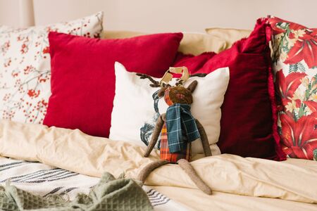 White and red pillows on the bed in the bedroom, stuffed deer toy among the pillows