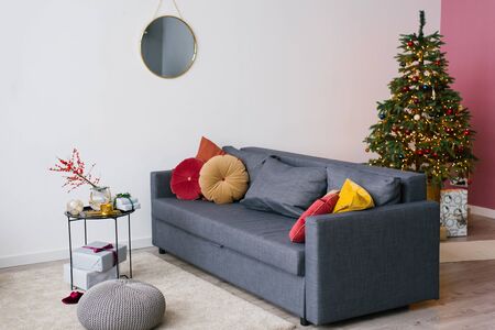 Dark gray sofa with bright red and yellow pillows, Christmas tree in the interior of the living room in the houseの写真素材