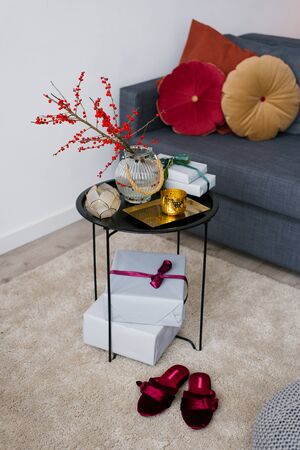 Decorative coffee table, decorated for Christmas or Thanksgiving, next to the Slippers are made of red velvet, gray sofa with bright pillowsの写真素材