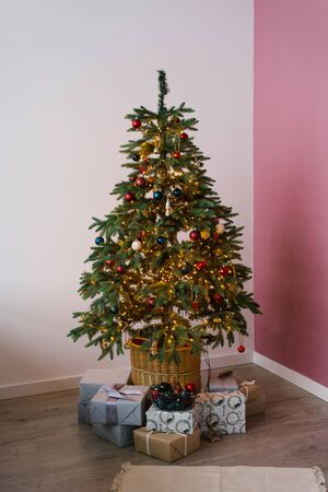 room Christmas tree decorated with red, white and emerald balls, gifts under the tree lie, Christmas room decor with white and pink wallsの写真素材