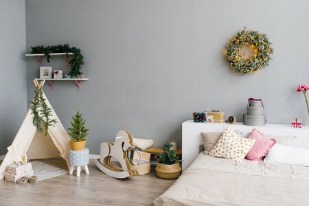 The interior of the bedroom or children's room decorated for Christmas or New Year: bed, wigwam, children's swing horse, Christmas wreath on the wallの写真素材