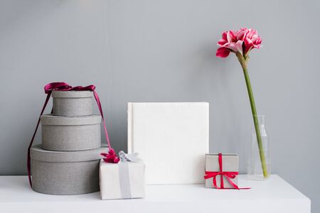 Photobook surrounded by gift boxes, gift and flower in vase on grey wall backgroundの写真素材