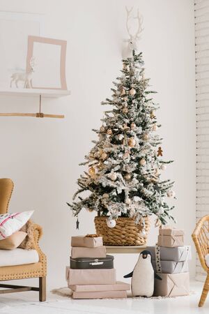 A beautiful Christmas tree with artificial snow stands in the living room in beige and light colorsの写真素材