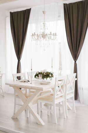 Bright dining set: a table with chairs in the bright living room is opposite the window, above the table hangs a white chandelierの写真素材