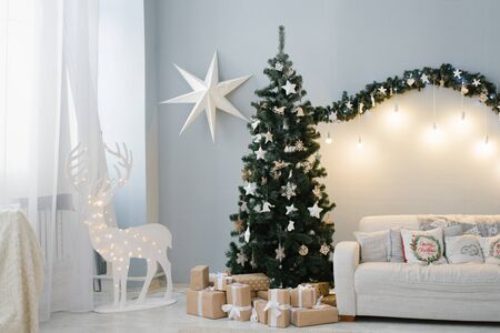 A beautiful Christmas tree stands in the interior of the living room with a sofa and a deer with lightsの写真素材
