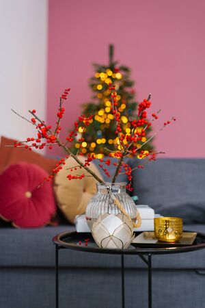 Branches with red berries in a glass vase are on the coffee table in the living room, decorated for Christmas and new yearの写真素材