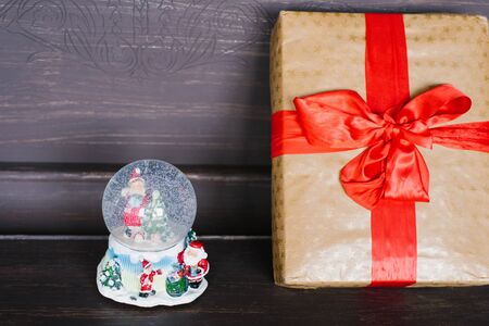 Souvenir glass Christmas snow globe and gift wrapped in Kraft paper with red ribbon and bowの写真素材