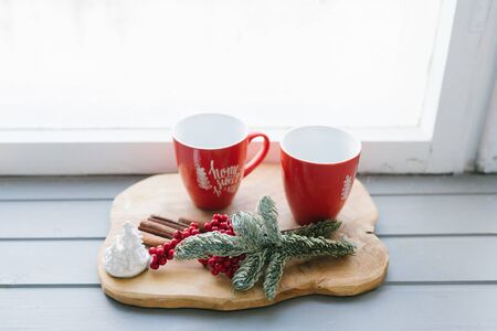 Red mugs with tea, coffee or mulled wine on the windowsill in the decor of a house or apartment, Scandinavian and home comfort at Christmasの写真素材