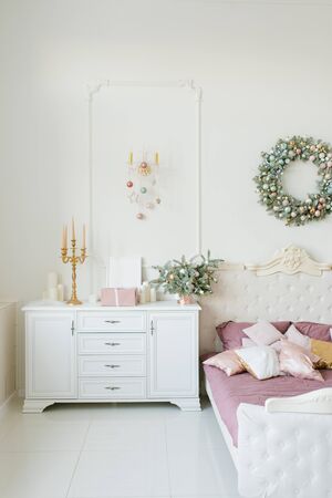 Stylish classic bedroom decorated for Christmas and New Year: a white chest of drawers, a bed and a Christmas wreath on the wallの写真素材