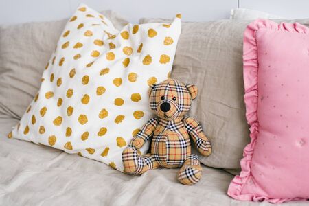 Soft toy plaid bear among pillows on the bedの写真素材