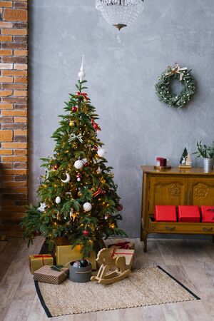 Traditional Christmas tree with gifts under it and a wooden classic chest of drawers in the living room in the loft style, decorated for Christmas and New Yearの写真素材