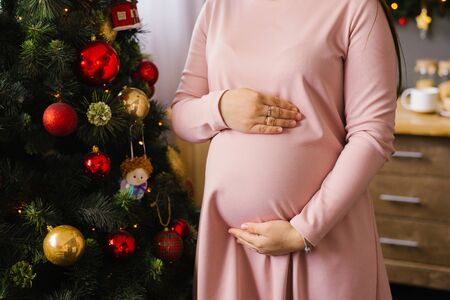 Woman holds hands on her pregnant belly on the background of Christmas tree lights.の写真素材
