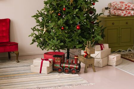 Christmas gift boxes, toy steam engine under the Christmas tree with lights in the living roomの写真素材