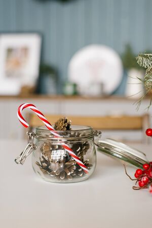 Glass jar with a lid filled with cones of conifer and a lollipop cane on the kitchen table decorated for Christmasの写真素材