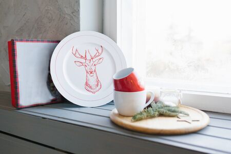 Christmas plate and mugs on the windowsill in the house
