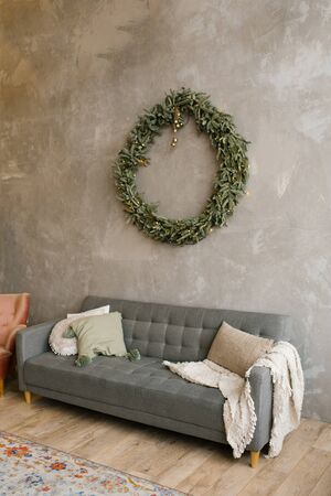 Gray sofa with pillows, over the sofa on the wall hangs a Christmas wreath. Scandinavian style in the living roomの写真素材