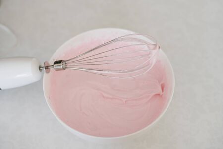 Pink cream in a bowl and whisk mixer on a plate