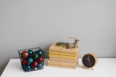 Books, Christmas toy deer, metal basket with Christmas tree colorful balls and table clock on a...