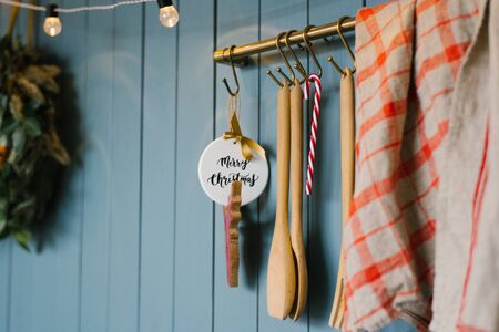Wooden kitchen spoon and toy with happy Christmas inscription, red grey towel on hooks in Scandinavian style kitchenの写真素材