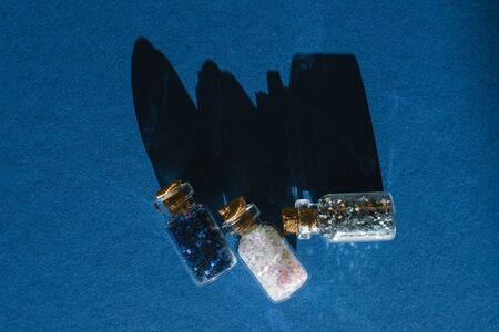 Glass jars with glitter or glitter on a blue background with hard shadow with copy space