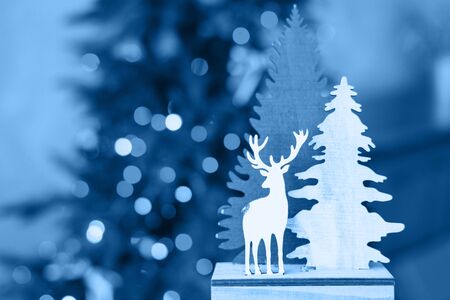 Classic Blue color of the year 2020. Christmas souvenir wooden Christmas trees and deer on the background of Christmas new year lights. Christmas holiday card. Copy spaceの写真素材