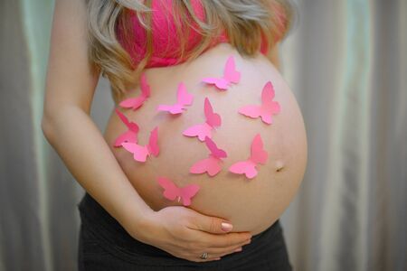 Pink paper butterflies on pregnant woman's belly close upの写真素材