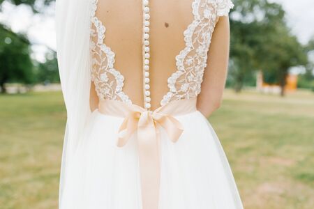 Open back beautiful bride dress with lots of white buttons and satin beige bow. Wedding detailsの写真素材