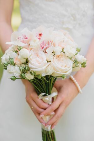 Delicate wedding bouquet of milk and white roses, orchids in the hands of the brideの写真素材